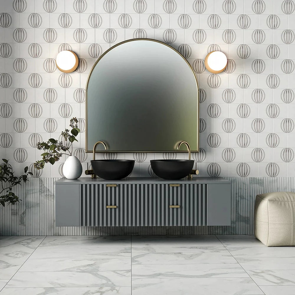 Modern bathroom with patterned wall tiles, large arched mirror, dual black sinks, gold faucets, gray floating vanity, marble floor tiles, round wall sconces.