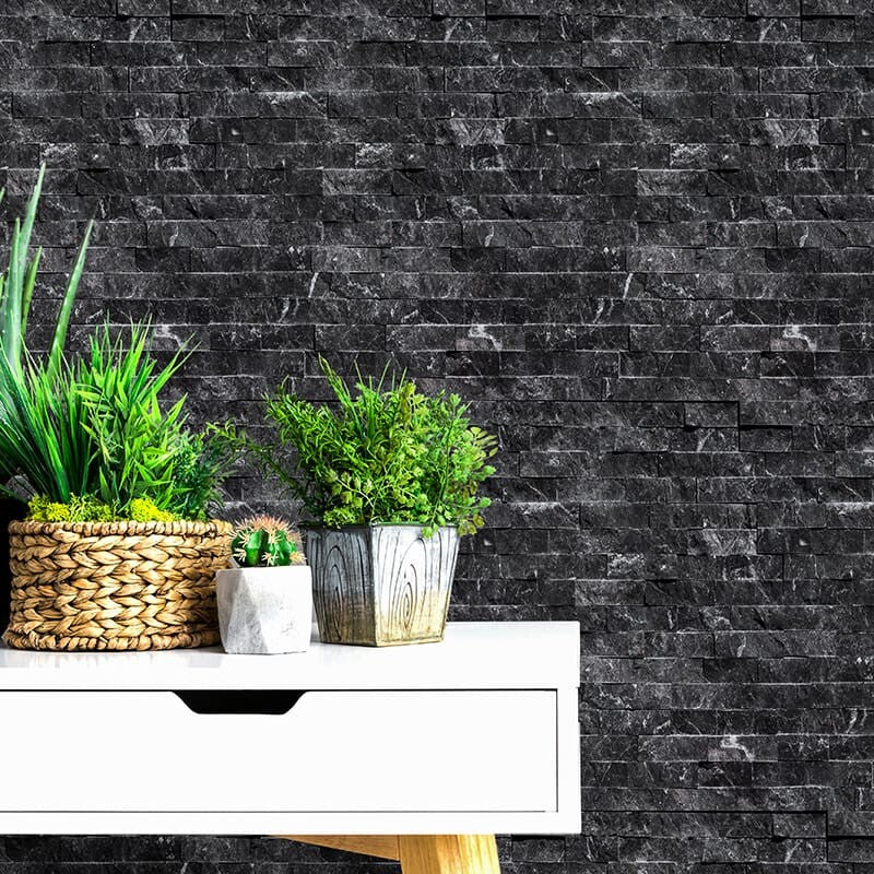 Wall with black marble tiles and flat rock texture. White table with wooden legs, potted plants in woven, metallic, and ceramic pots.