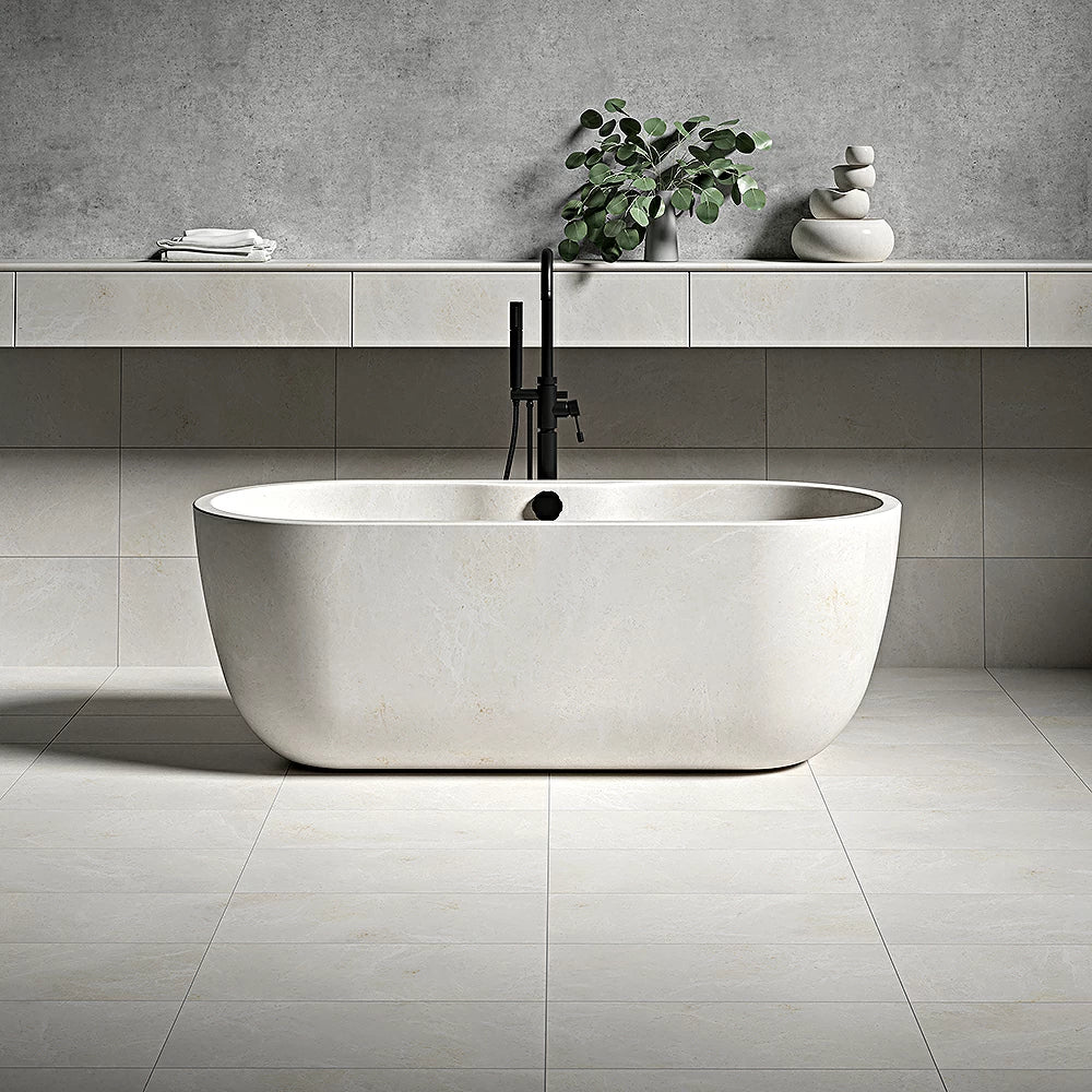 Modern bathroom with white bathtub, vanilla marble tiles, gray concrete wall, black faucet, potted plant, and stacked stones on a shelf.