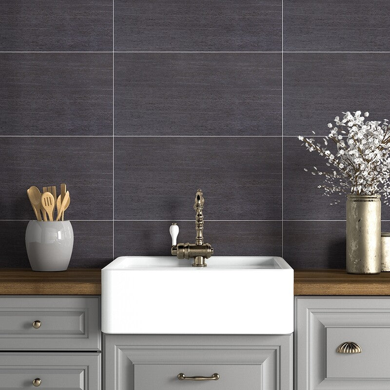 Modern kitchen with dark matte rectangular tiles, wooden countertop, farmhouse sink, brass faucet, gray vase with utensils, metallic vase with flowers, light gray cabinetry.