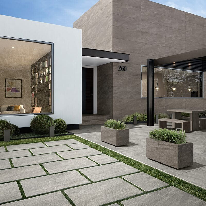 Modern outdoor patio with grey slate tiles, grass pathways, planters, contemporary seating, and sleek house backdrop.