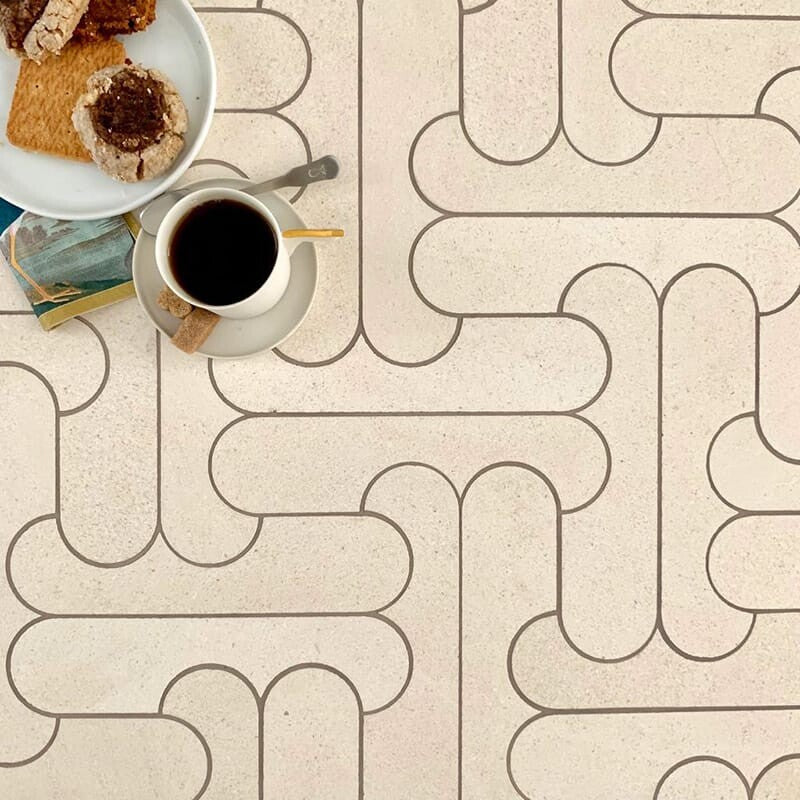 Top view of geometric tiled surface with cookies, coffee, spoon, and books. Neutral tones, inviting atmosphere.
