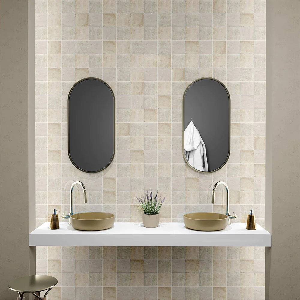 Beige Moroccan Zellige tiles, double oval mirrors, white floating vanity, round vessel sinks, brass faucets, lavender plant in center.