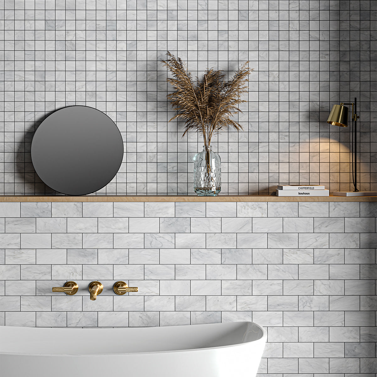Modern bathroom with white marble subway tiles, wooden shelf with round mirror, dried plant vase, gold lamp, and small gray wall tiles.