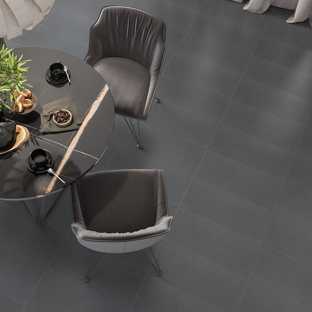 Modern dining area with dark gray tile flooring, round black dining table, chairs, and plant centerpiece.