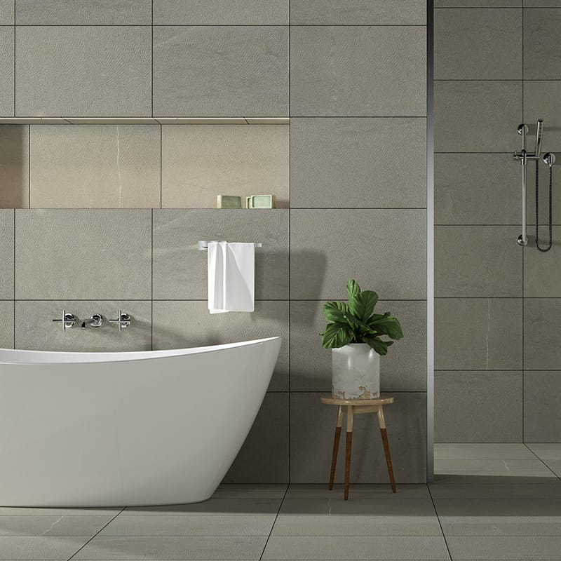 Contemporary bathroom with limestone tiles, white freestanding tub, toiletries shelf, towel, and potted plant on wooden stool.