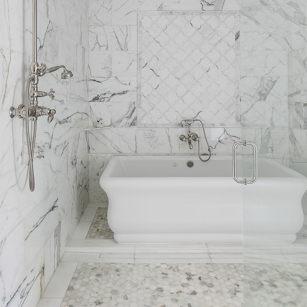 Luxurious bathroom with Calacatta gold marble tiles, white freestanding bathtub, glass shower enclosure, and silver fixtures.