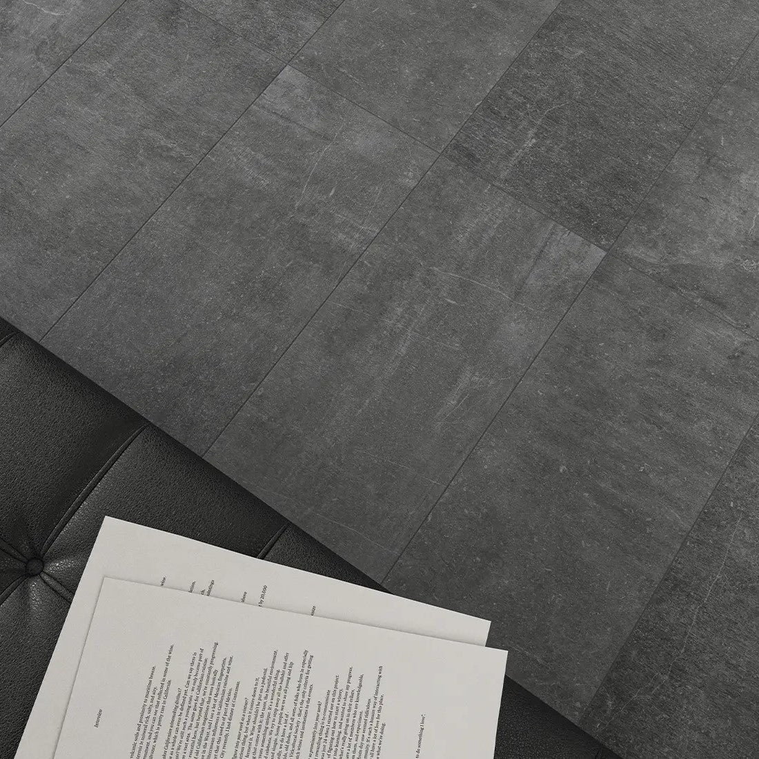 Dark grey, large-format porcelain tiles with a contemporary look and a subtle stone texture, extending across a floor with a partial view of a book or magazine on one side.