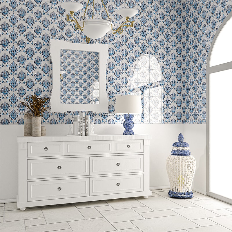 White dresser with silver handles, blue/white tile walls, mirror, table lamp, ceramic jar, chandelier in room.
