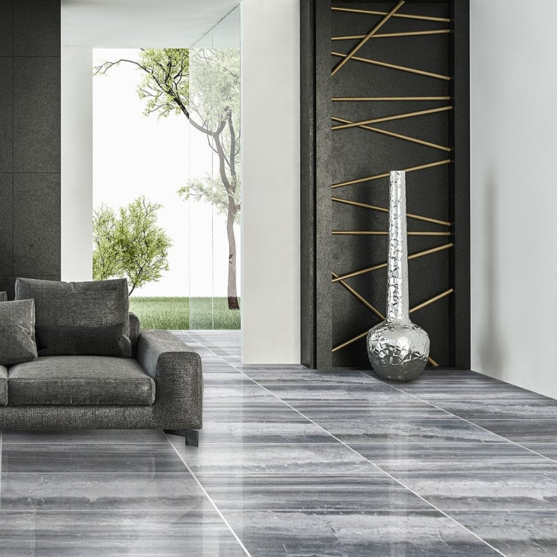 Modern living room with Haisa Black Marble tiles, grey sofa, silver vase, black accent wall with gold accents, and large windows with greenery view.