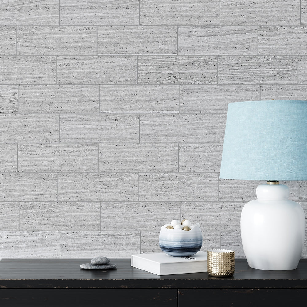 Wall with light gray marble tiles, wooden table with lamp, bowl, book, stones. Subtle striations add texture to the space.