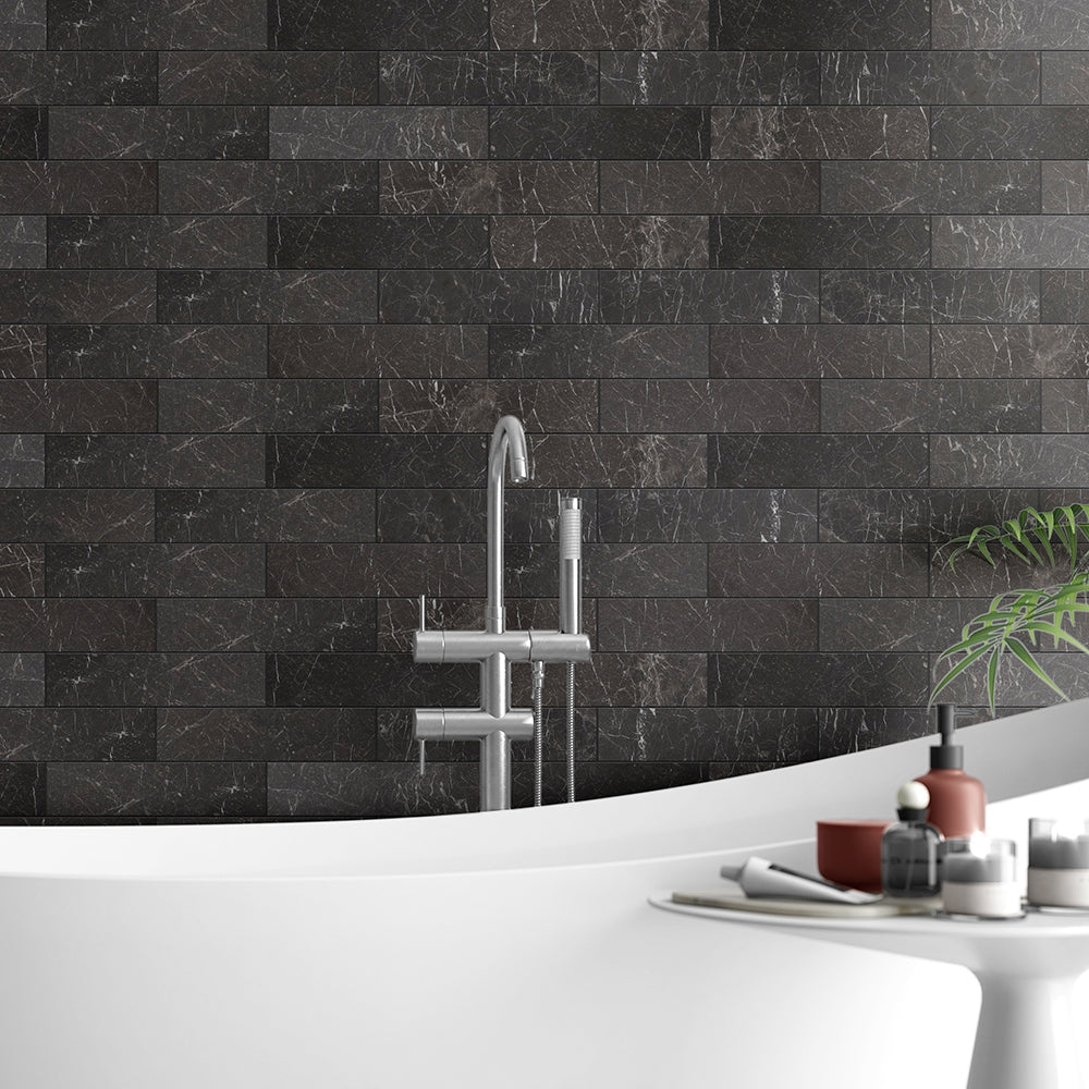 Luxurious bathroom with black marble tile wall, modern stainless steel faucet, white freestanding bathtub, and decorative items.