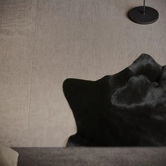 A wall and floor covered with linen-textured porcelain tiles in a soft beige color, with a dark textured rug on the floor partially visible.