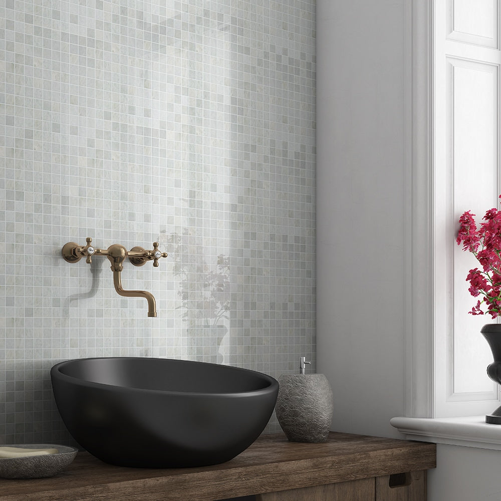 Modern bathroom with green and white mosaic tile backsplash, black vessel sink, brass faucet, wooden countertop, vase, and bowl.