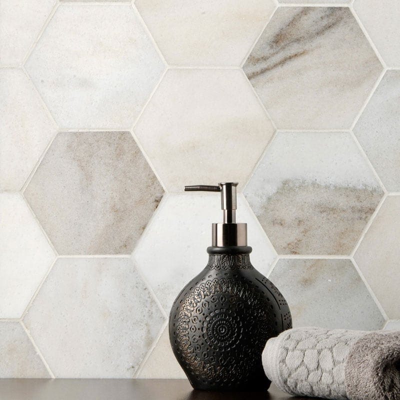 Hexagonal marble tiles in white and gray with natural veining, black soap dispenser, gray towel on dark surface in foreground.