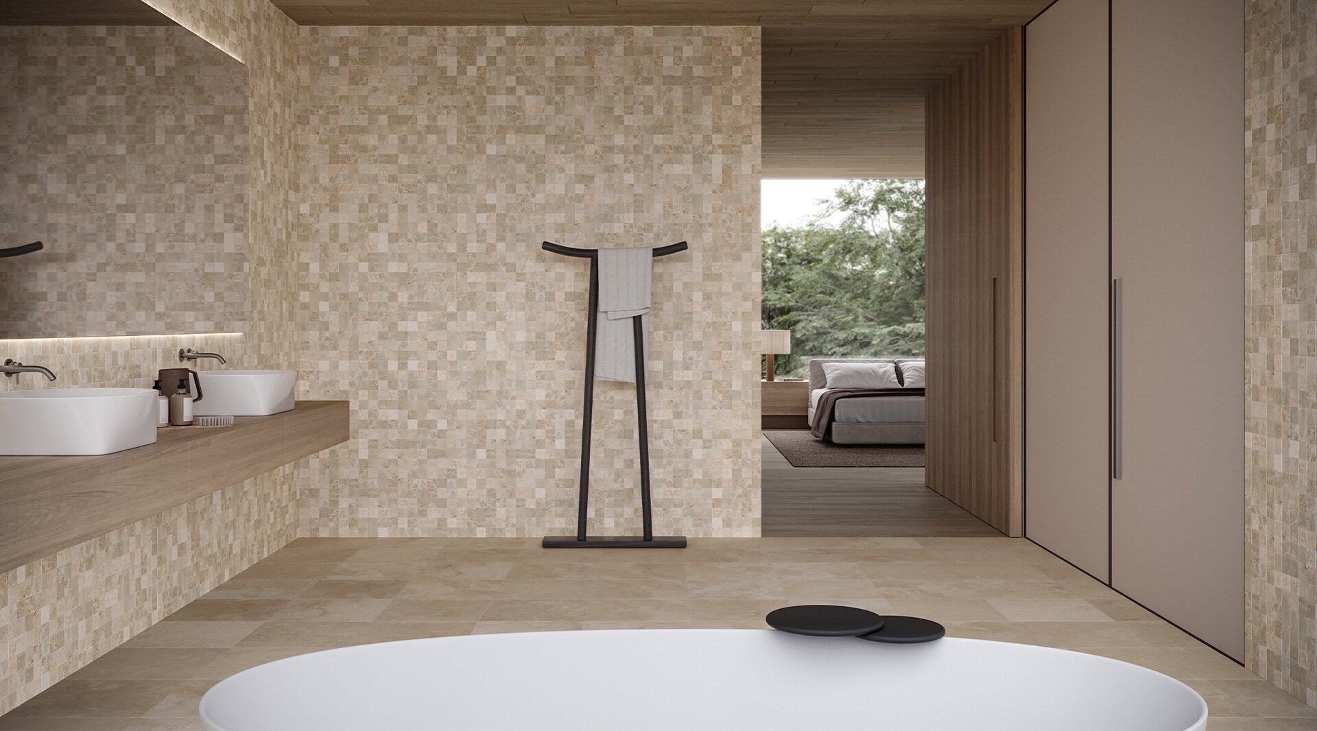 Modern bathroom with beige travertine tile, large wall mirror, double sinks with wooden countertops, black towel rack, and view into bedroom with natural light.