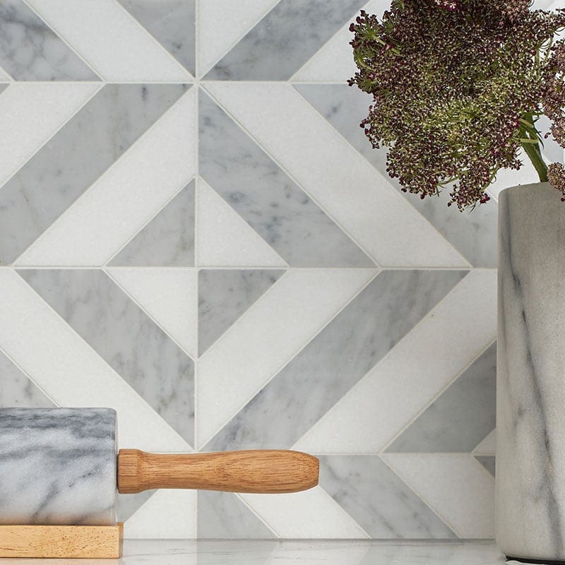 Close-up of white and gray marble tile wall, marble rolling pin with wooden handle, marble vase with green and purple flowers.