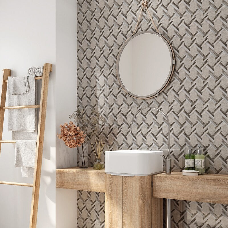 Bathroom scene with wooden vanity, round mirror, white sink, braided hexagon mosaic tile wall, ladder with towels, shelf with essentials.