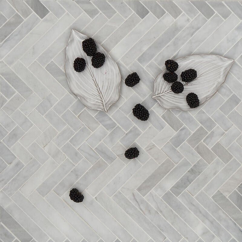 Avenza herringbone mosaic tile in light gray/white, honed finish. Ceramic leaf dishes with blackberries on top.