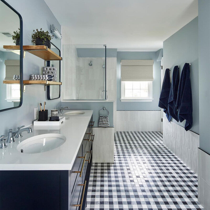 Modern bathroom with black and white checkered tile, light blue walls, double sink vanity, frameless mirror, open shelves, glass shower, and blue towels.