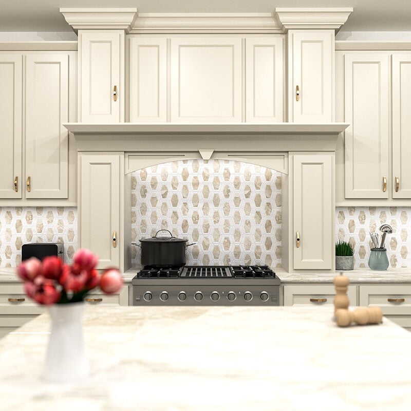 Elegant cream-colored kitchen with intricate molding, hexagonal marble backsplash, stainless steel gas stove, white marble countertop, bright & sophisticated.