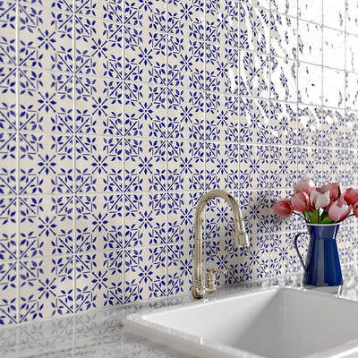 Blue and white square tiles on wall with silver faucet; navy blue vase with flowers on right of sink.