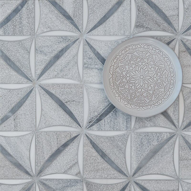 Marble tile mosaic with interlocking circles & diamonds in white & gray, adorned with a decorative plate displaying intricate geometric design.