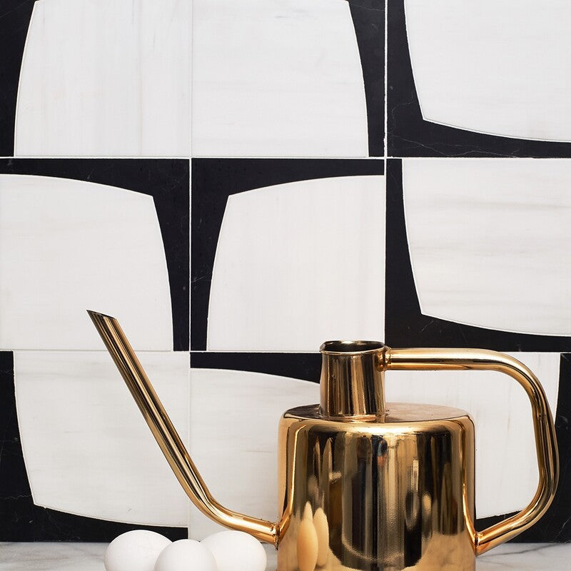 Black and white geometric tiles in a mosaic pattern on wall, gold watering can, white eggs on white surface - modern and stylish composition.