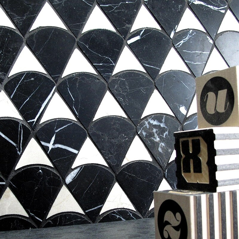 Modern black and white mosaic wall with scales pattern, honed marble tiles, and wooden alphabet blocks on black surface.