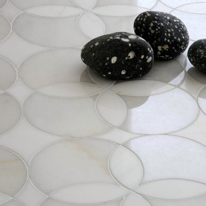 Close-up of a white marble tile mosaic with a circular pattern, featuring a multi-finish texture. Three polished black stones with white speckles.