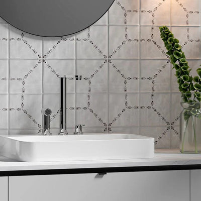 Stylish bathroom with white and gray tiles, modern sink and tall faucet. Counter has glass vase, candle, soap dispenser, and bottle.